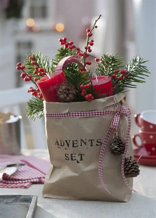 Коричневый бумажный пакет, украшенный ветками, свечами и сосновыми шишками.