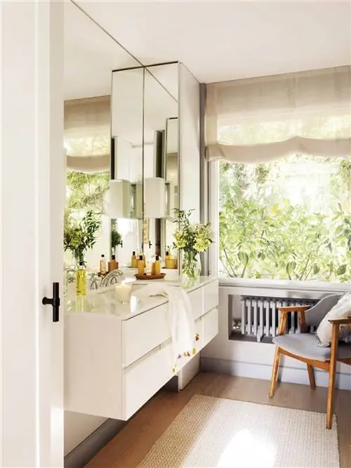 Современная ванная комната с подвесным белым шкафом и окном со шторкой.