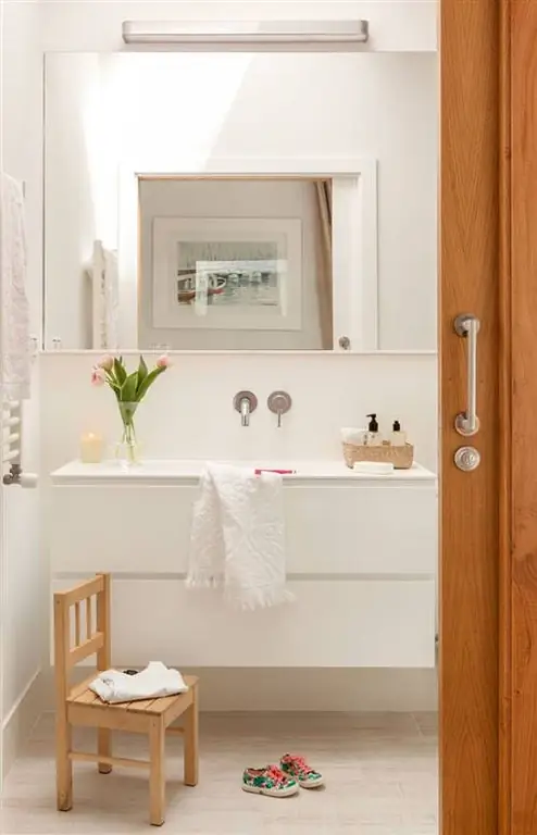 Ванная комната с подвесным белым шкафом и большим зеркалом с настенным светильником.