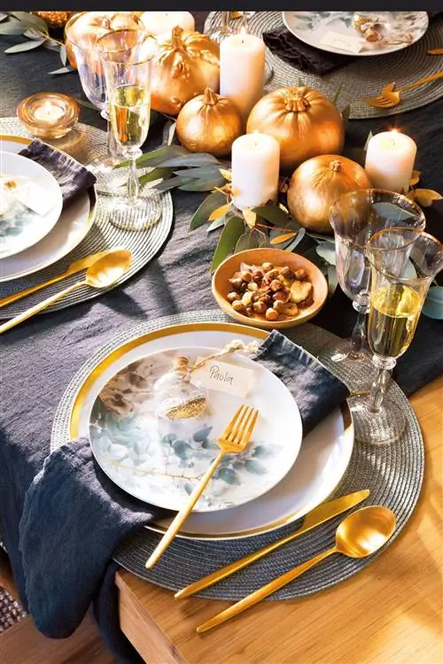 Стол, накрытый к Рождеству, с узорчатыми тарелками и золотыми столовыми приборами.
