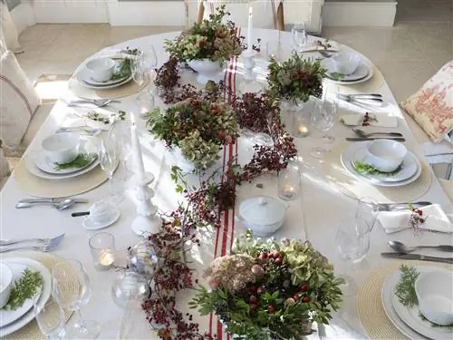 Сервировка рождественского стола с гирляндами красного падуба.