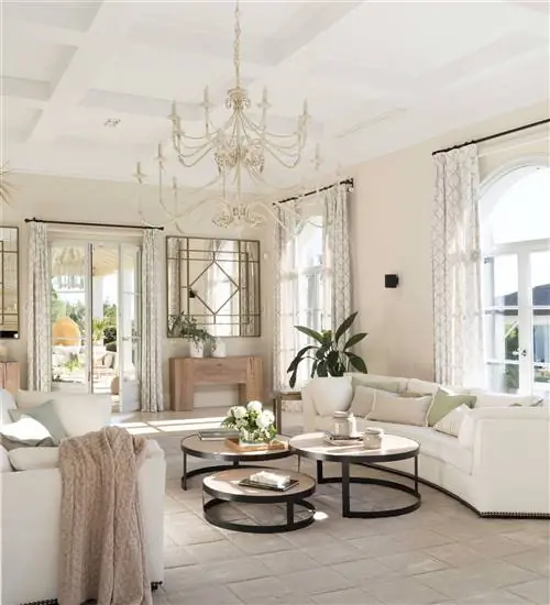 Величественная гостиная с изогнутыми белыми диванами, потолочной лепниной и люстрой.