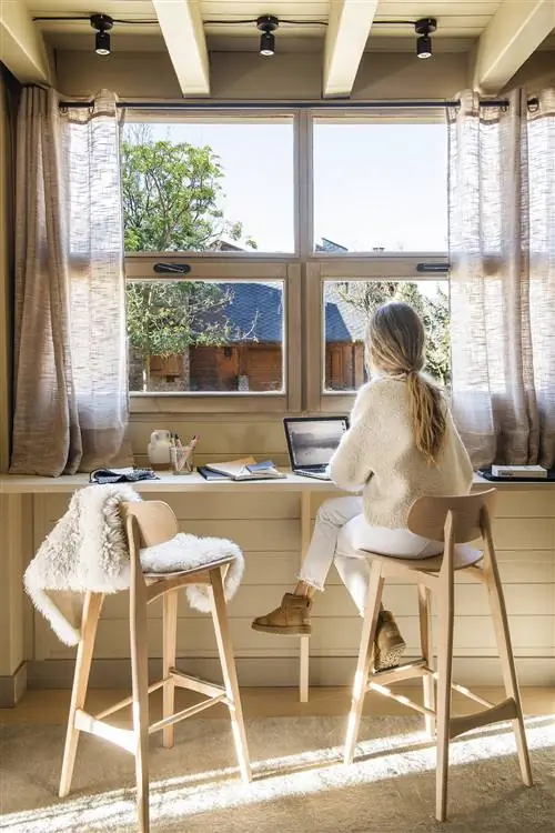 Рабочая зона с обшивкой, деревянным столом и табуретками перед окном.