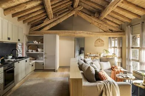 Кухня открыта для гостиной и столовой с деревянными балками на потолке и перегородкой за диваном.