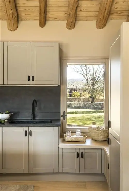 Деревенская кухня с каменной мебелью, потолочными балками и окном.