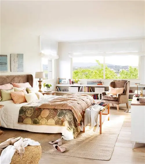 Большая спальня с окном, низким шкафом и креслом.