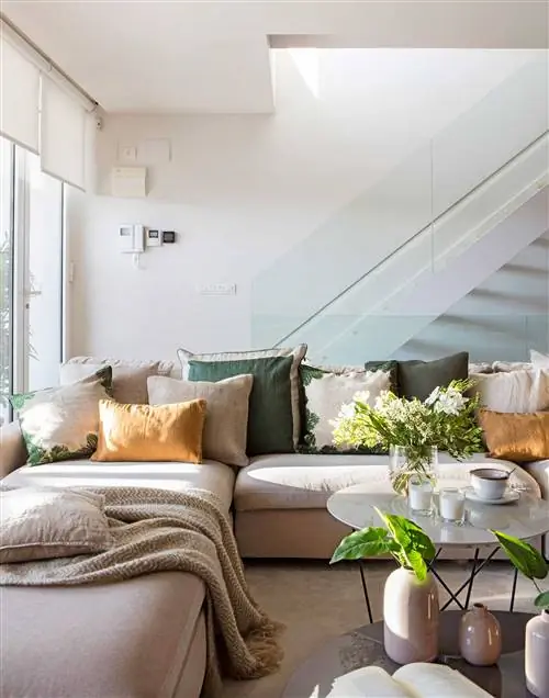 Гостиная с серым диваном с подушками и лестницей со стеклянными перилами.