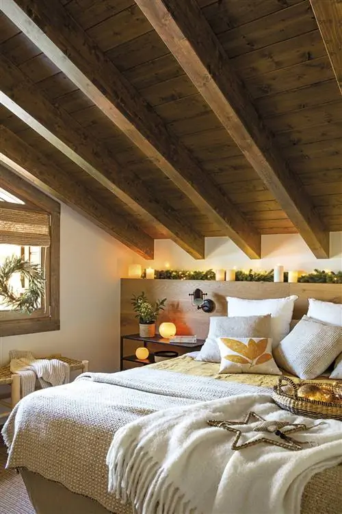 Спальня в деревенском стиле с деревянными балками, рождественскими украшениями и изготовленным на заказ изголовьем со свечами и гирляндой.