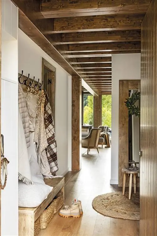 Холл в деревенском стиле с деревянными балками, скамейкой с вешалкой и ковриком из волокна.