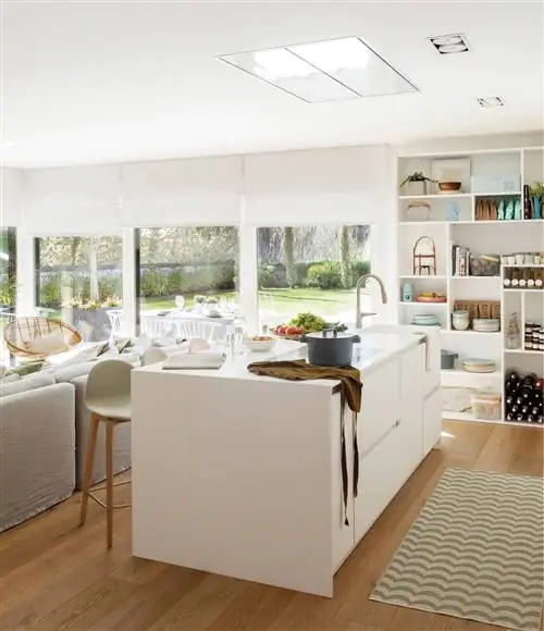 Белая кухня с островом, табуретками и стеллажами от пола до потолка в качестве кладовой.