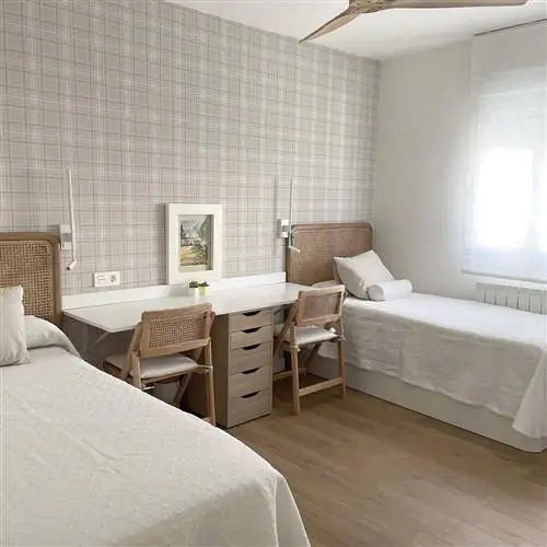 Комната после ремонта с обоями, белым письменным столом, двумя кроватями и окном со шторкой.