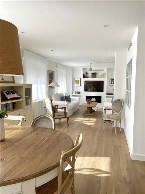 Гостиная после ремонта с камином, деревянным журнальным столиком, белым диваном и белой картиной.