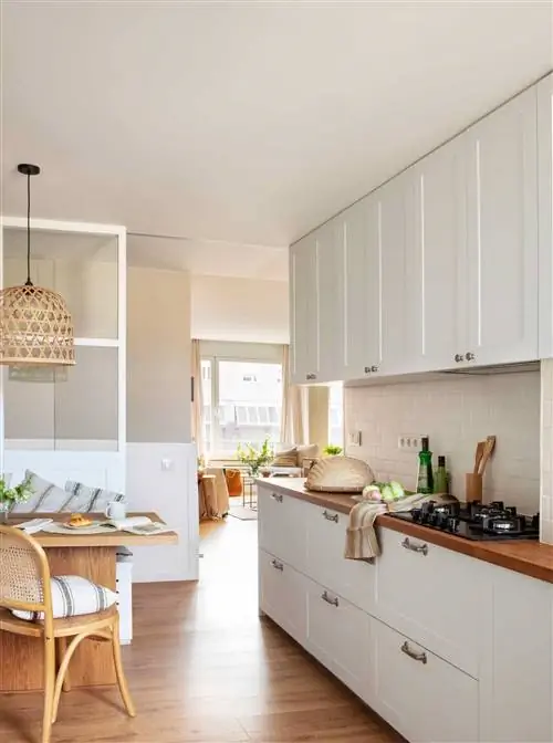 Кухня с белой мебелью, деревянной столешницей и раздвижной стеклянной дверью.