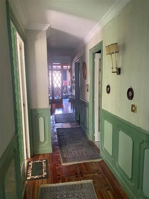 Перед холлом с зелеными панелями и обоями на стенах.