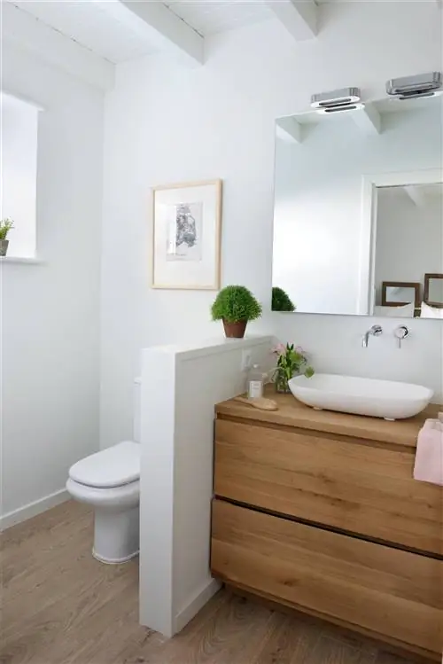 Ванная комната с деревянной мебелью и стеной на половину высоты, которая отделяет туалет.