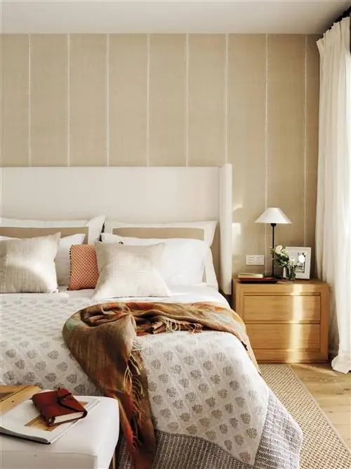 Спальня с бежевым изголовьем крыла, деревянной тумбочкой и полосатыми обоями.