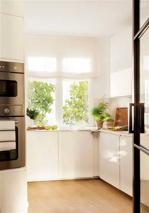 Небольшая угловая кухня с белой мебелью.