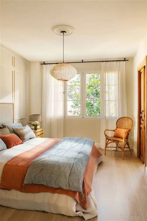 Спальня украшена потолочной лампой, креслом и кроватью со стеганым пледом.