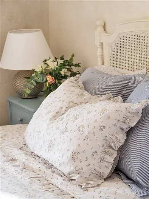 Белое постельное белье с желтыми цветами и рюшами и синие наволочки.