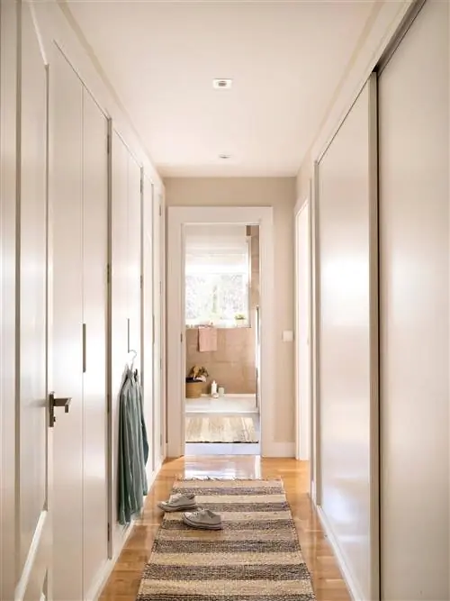 Длинная прихожая со шкафами и белыми лакированными дверями.