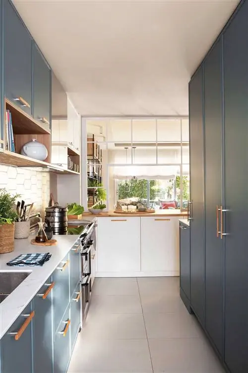 Узкая и вытянутая кухня с облицовочной мебелью синего цвета.