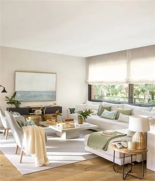 Гостиная с угловым диваном, креслом и ковром, оформленным в белом цвете и с деревом.