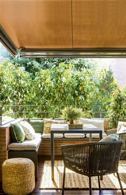 Терраса с кирпичными стенами, железным столом и скамейкой и ковром из натурального волокна.