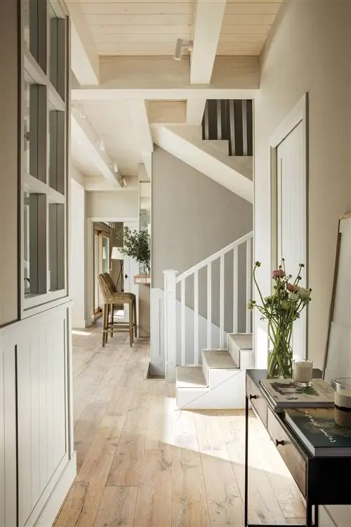 Вестибюль с консолью, пол из натурального дуба и белая деревянная лестница со ступенями, покрытыми синтетическим ковром из сизаля.