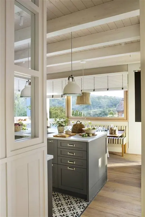 Кухня с островом насыщенного серого цвета с выдвижными ящиками и выдвижными ящиками. На заднем плане кабинет с полосатой мягкой скамьей.