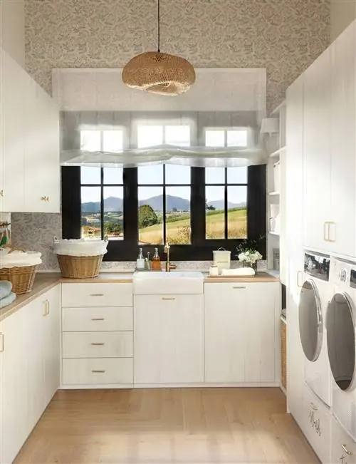 Прачечная с белыми шкафами, стиральной машиной и сушилкой, окном и корзинами.
