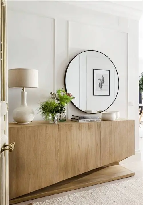 Современный зал с деревянным буфетом и круглым зеркалом.