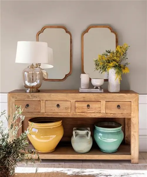 Керамическая ваза и эмалированные глиняные горшки стоят на деревянном буфете в холле.