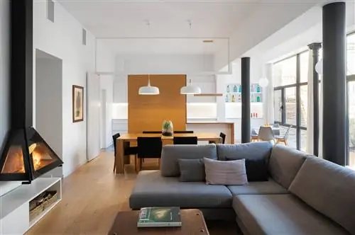 Гостиная и столовая после ремонта с серым диваном, современным камином и деревянным столом с черными стульями.