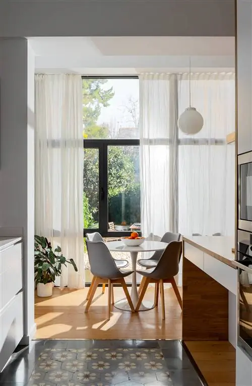 Офис после ремонта с белым круглым столом и серыми современными стульями у окна.