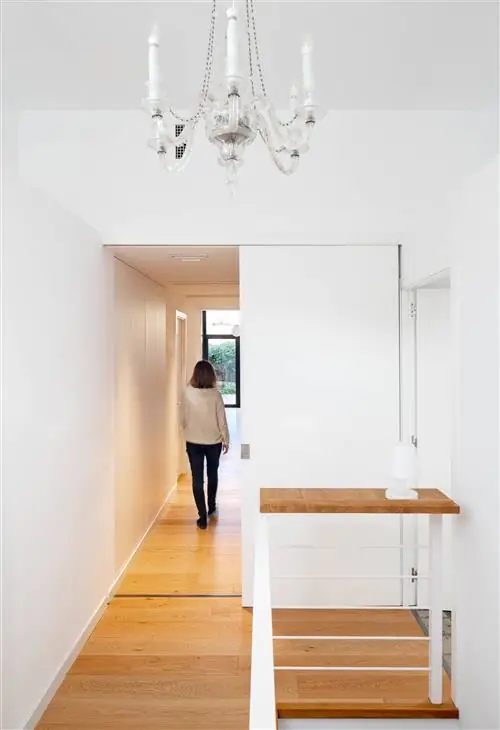 Прихожая после ремонта с деревянными полами, белыми стенами и люстрой на потолке.