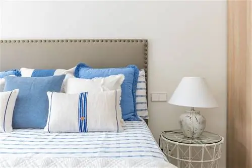 кровать с серым изголовьем с заклепками и синими подушками