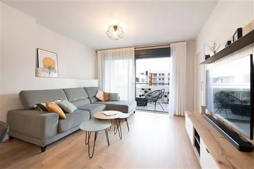 гостиная с серым мягким диваном с козеткой, встроенными столами и выходом на террасу