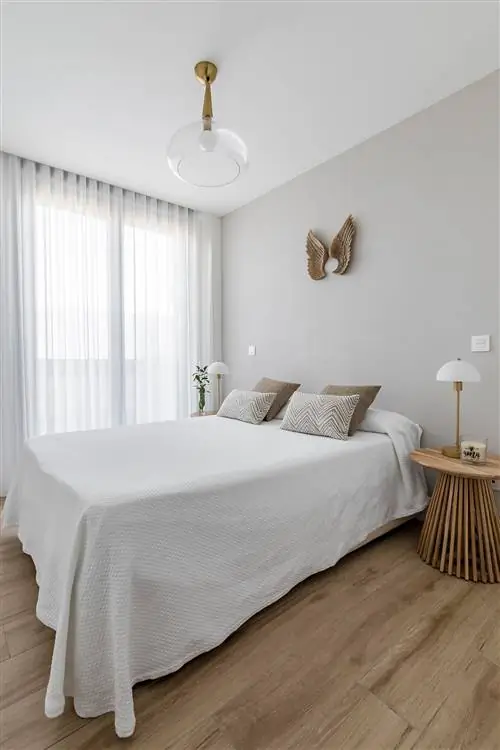 спальня оформлена в нейтральных тонах с деревянной тумбочкой и фигуркой ангельских крыльев на изголовье