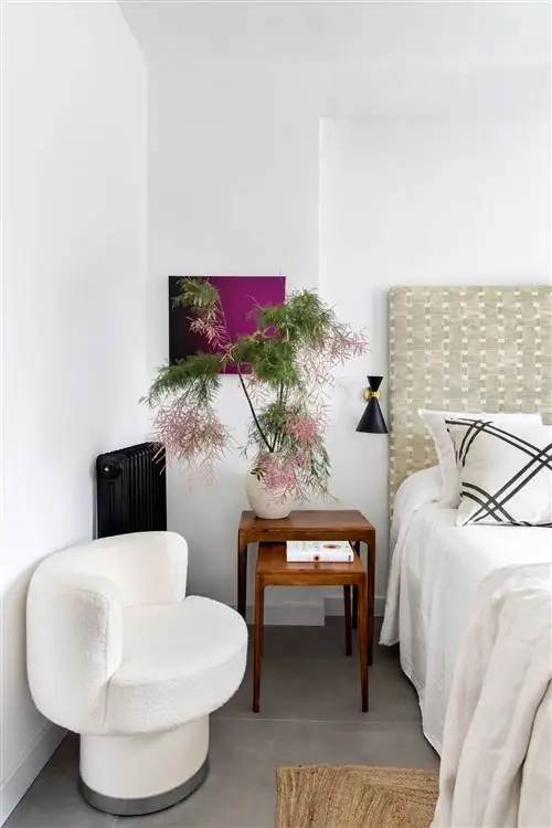 спальня с плетеным изголовьем, деревянными раскладными столиками, современным креслом с белой обивкой из букле и ковром из волокна