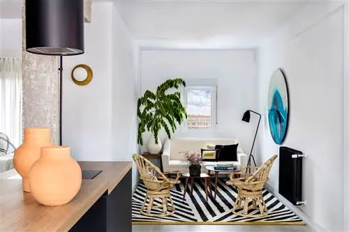 гостиная открытой планировки с белым диваном, двумя креслами из ротанга, деревянными столами и ковром в черно-белую полоску