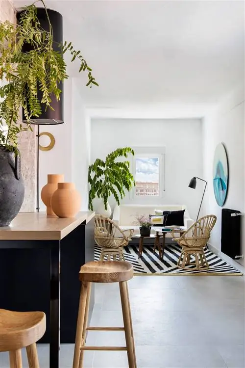 гостиная открытой планировки с белым диваном, двумя креслами из ротанга, деревянными столами и ковром в черно-белую полоску