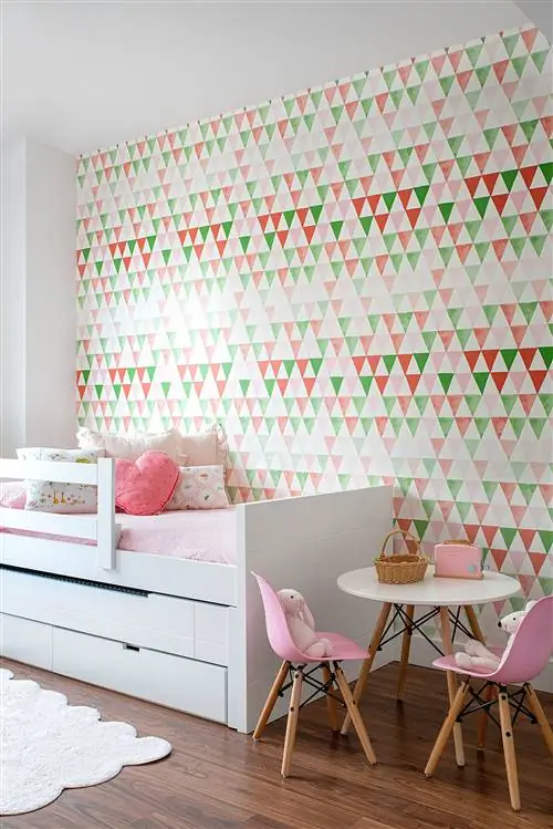 детская спальня с белой раскладной кроватью, белым столом и розовыми стульями, а также розово-зелеными геометрическими обоями