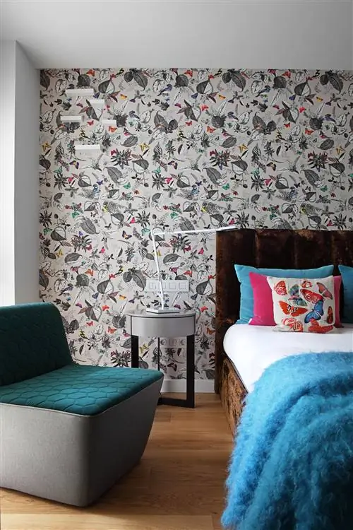 спальня с экзотическими узорчатыми обоями на стене изголовья, коричневой бархатной кроватью и современным креслом