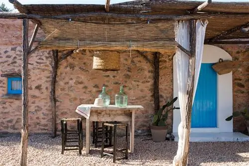 веранда с высоким деревянным столом и табуретами из дерева и волокна в средиземноморском стиле с ротанговой мебелью с цветными подушками