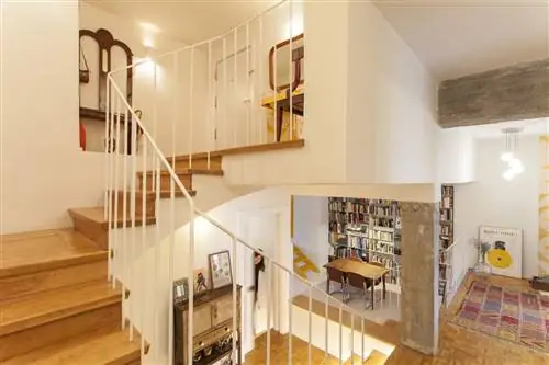 лофт с бетонными балками и колоннами и деревянной лестницей с перилами из белого металла