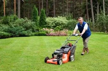 Старший мужчина косит газон.