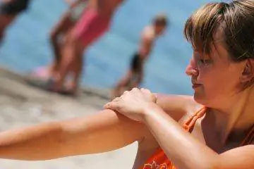 Женщина наносит солнцезащитный крем на пляж.