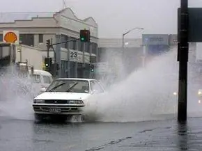 Автомобили разбрызгивают воду в центре Окленда, Новая Зеландия, когда они едут по глубоким лужам во время сильного дождя.