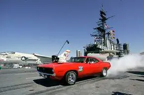 Chevrolet Camaro сжигает свои шины вместе с истребителем ВМС во время демонстрации в кабине экипажа авианосца USS Midway в Сан-Диего, Калифорния.