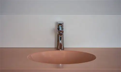 Крупный план розовой керамической раковины с современным краном в ванной.